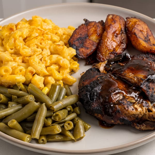 A plate of jerk chicken with mac and cheese, green beans, and fried plantains.